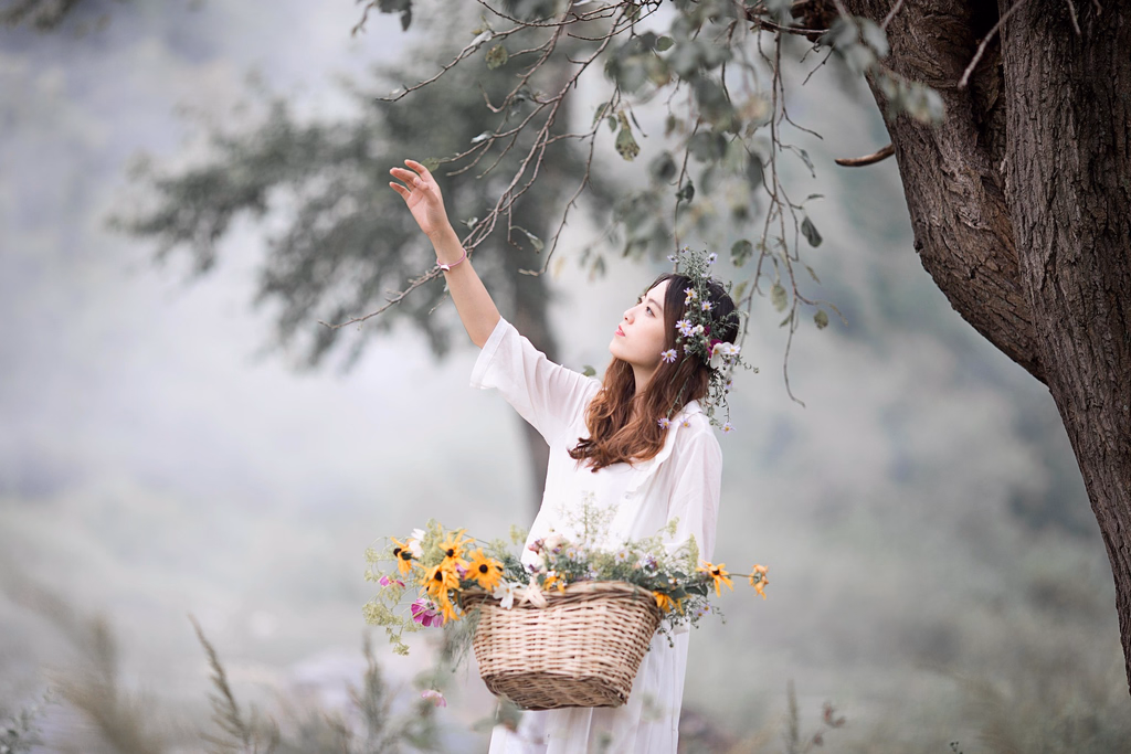 AVIF to WebP converter, before: a woman in white with a basket of flowers reaching up to a branch in soft mist, AVIF, 142.2 KB