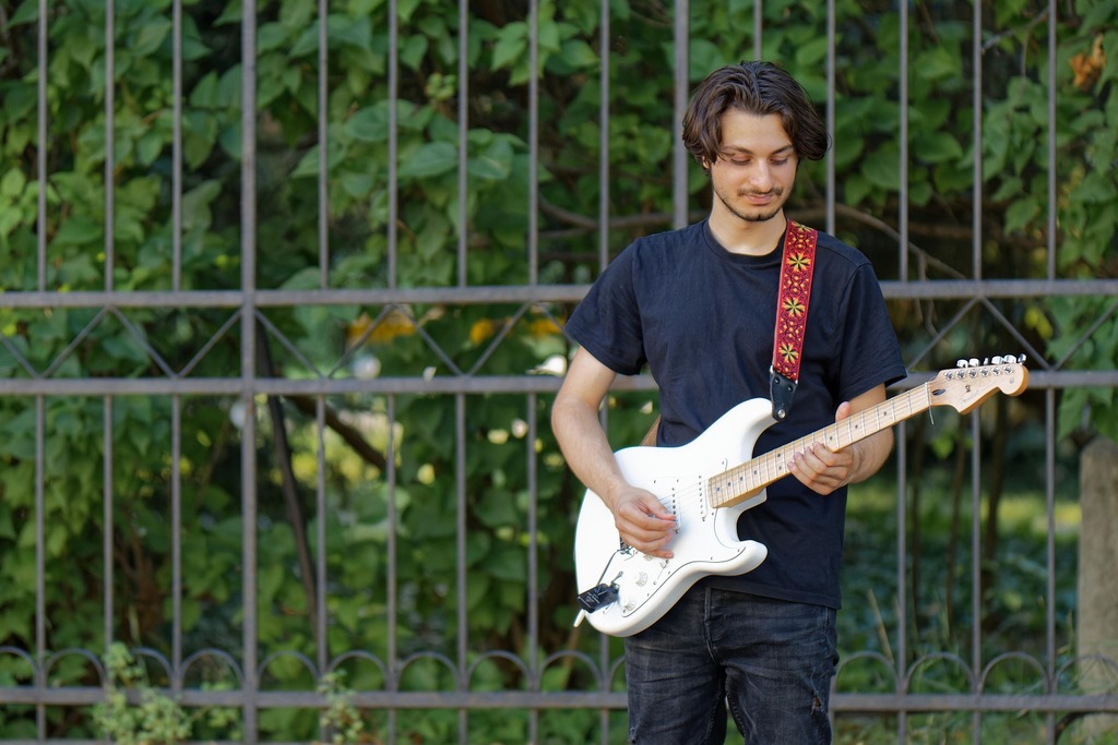 Flip image online, before: a young man playing a white electric guitar in front of a green fence, Original, 164.3 KB