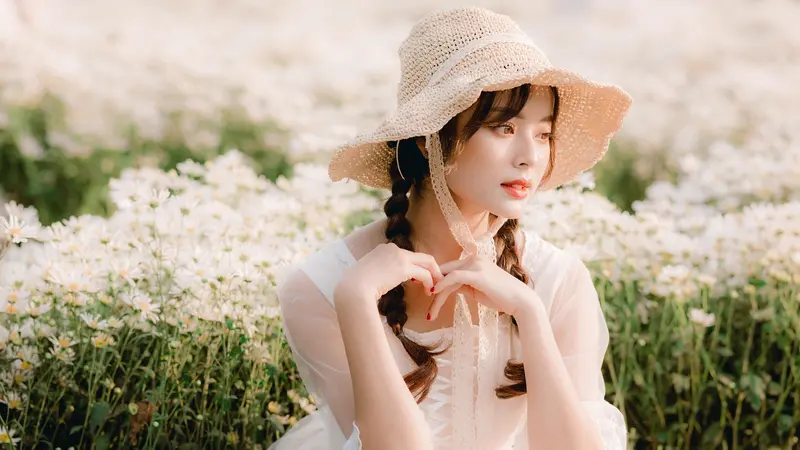 A woman in a straw hat resting her chin on her hands among white flowers