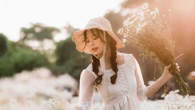 A woman in a straw hat holding dried flowers in warm backlight