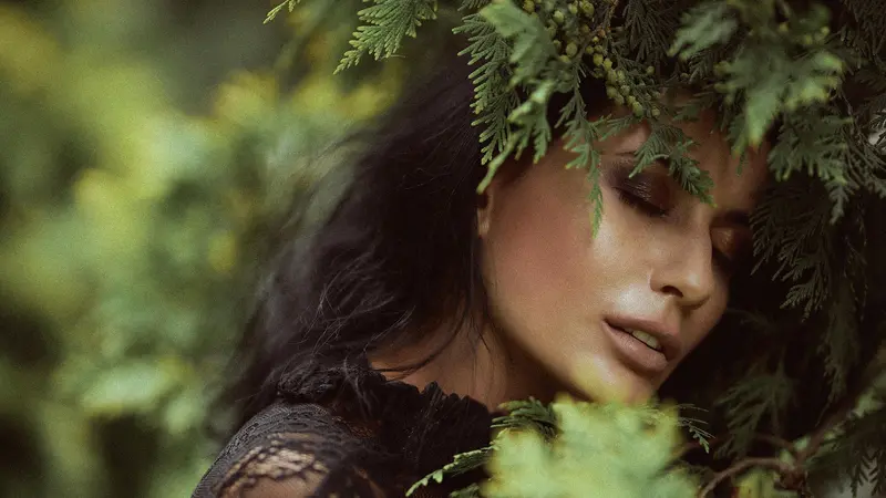 A woman with her eyes closed, her face framed by fern leaves