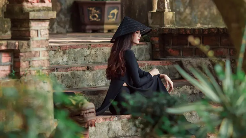 A woman in black with a conical hat sitting on old temple steps